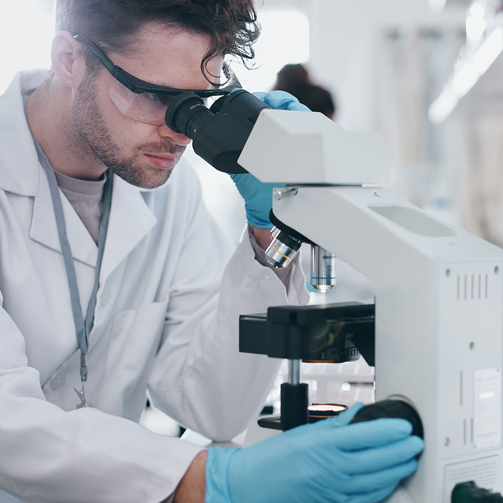 Man in white coat and blue gloves looking into a microscope