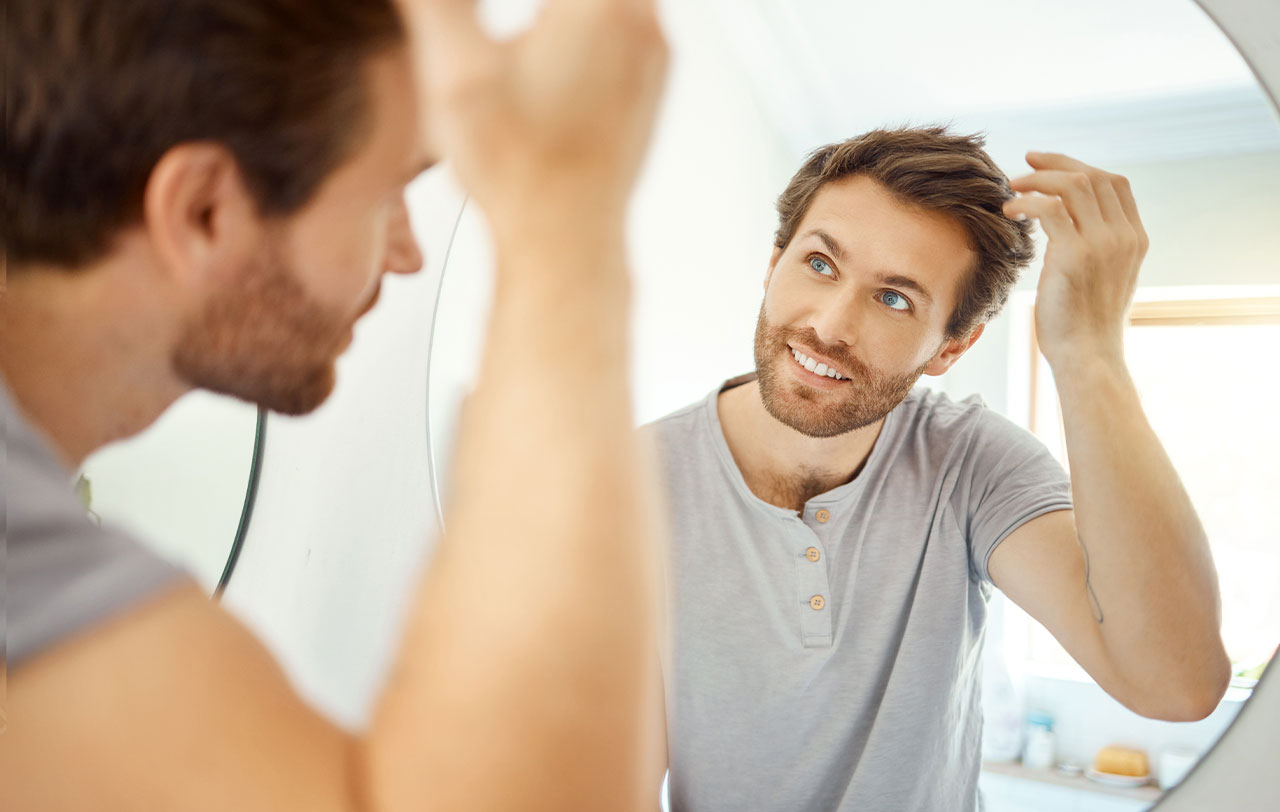 Young man in grey shirt looking in the mirror at his hair