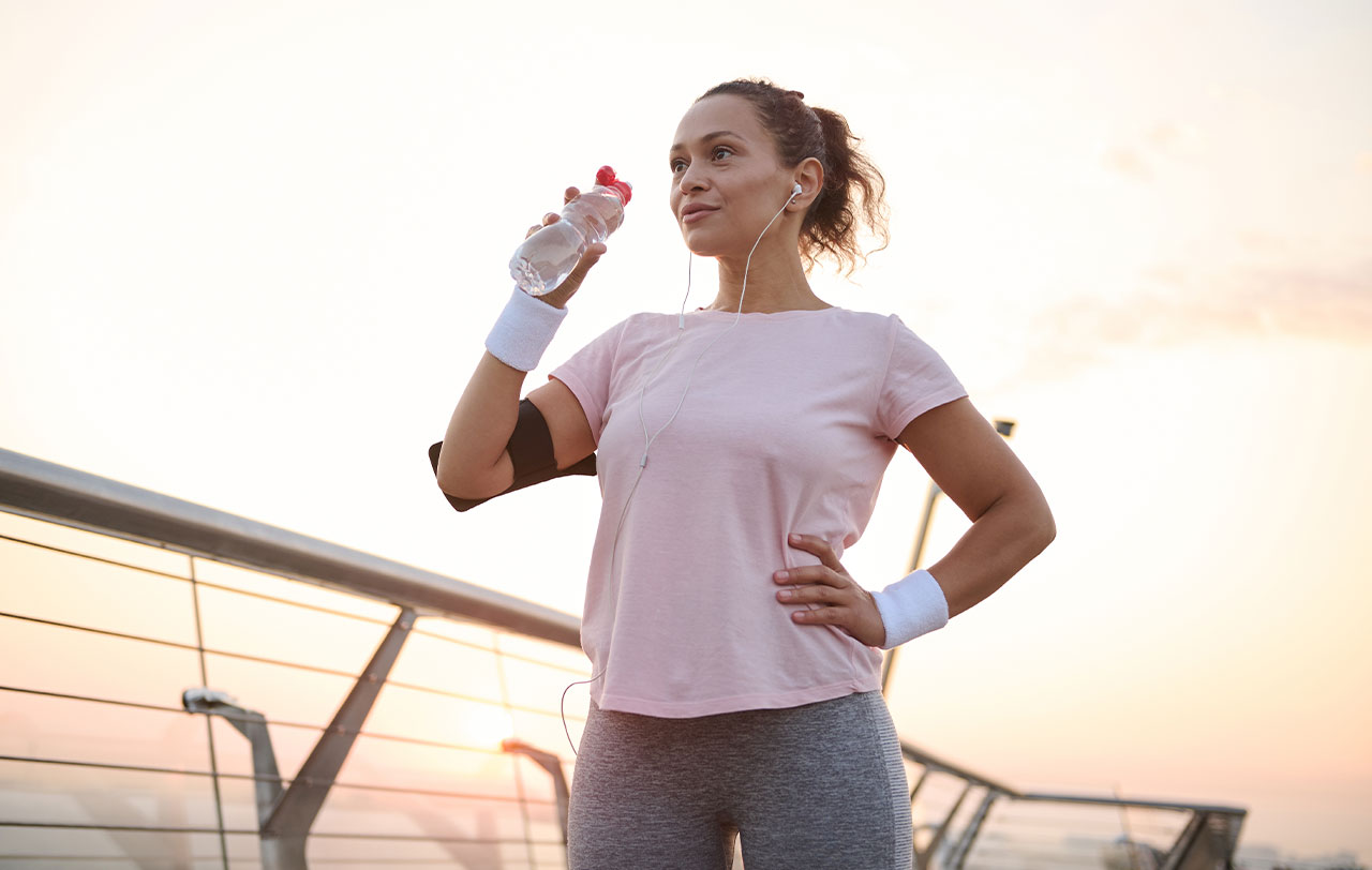 Athletic woman in pink shirt drinking from a water bottle after a workout.